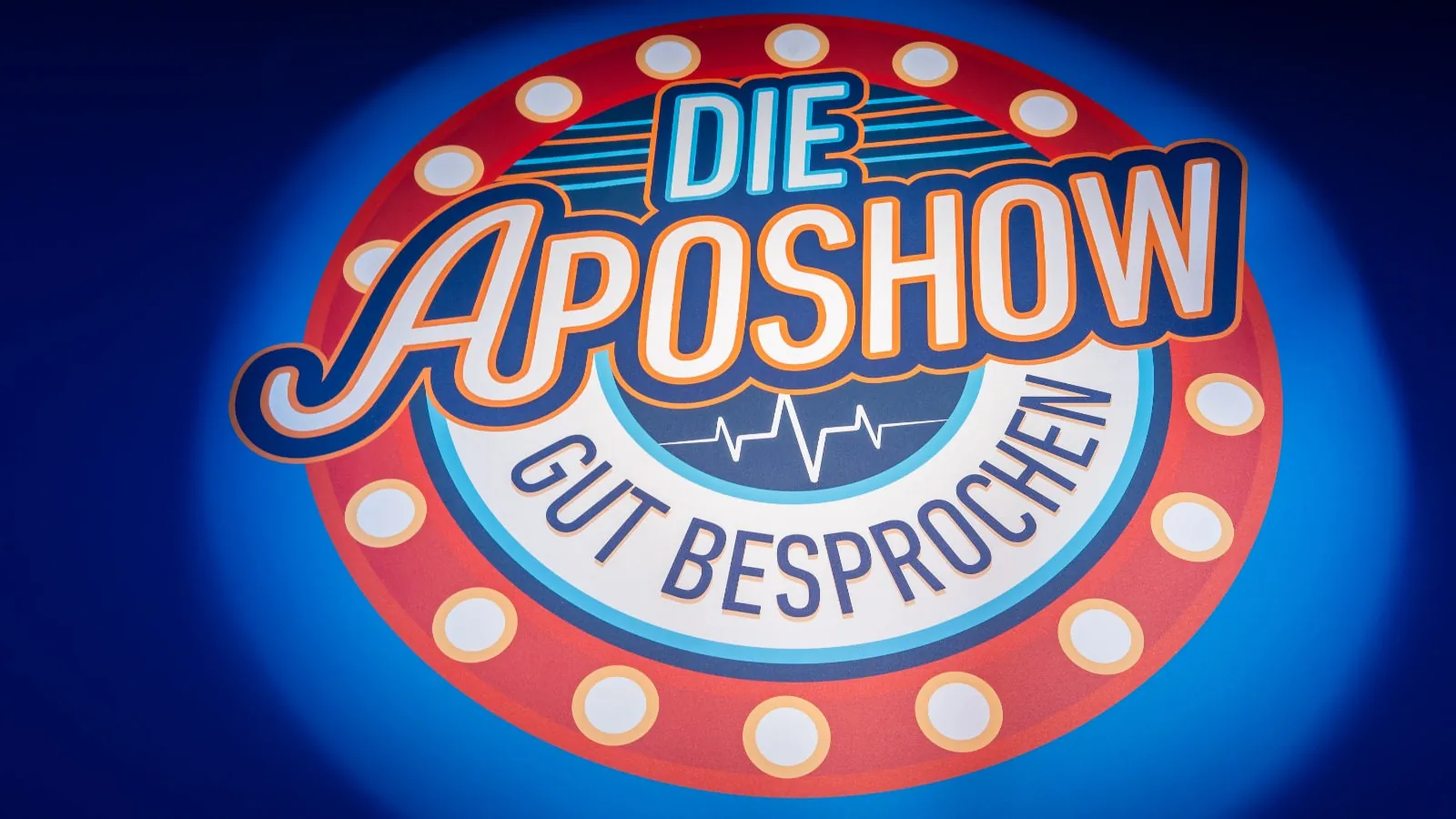 Logo „Die ApoShow – Gut besprochen“ im Spotlicht auf blauem Grund