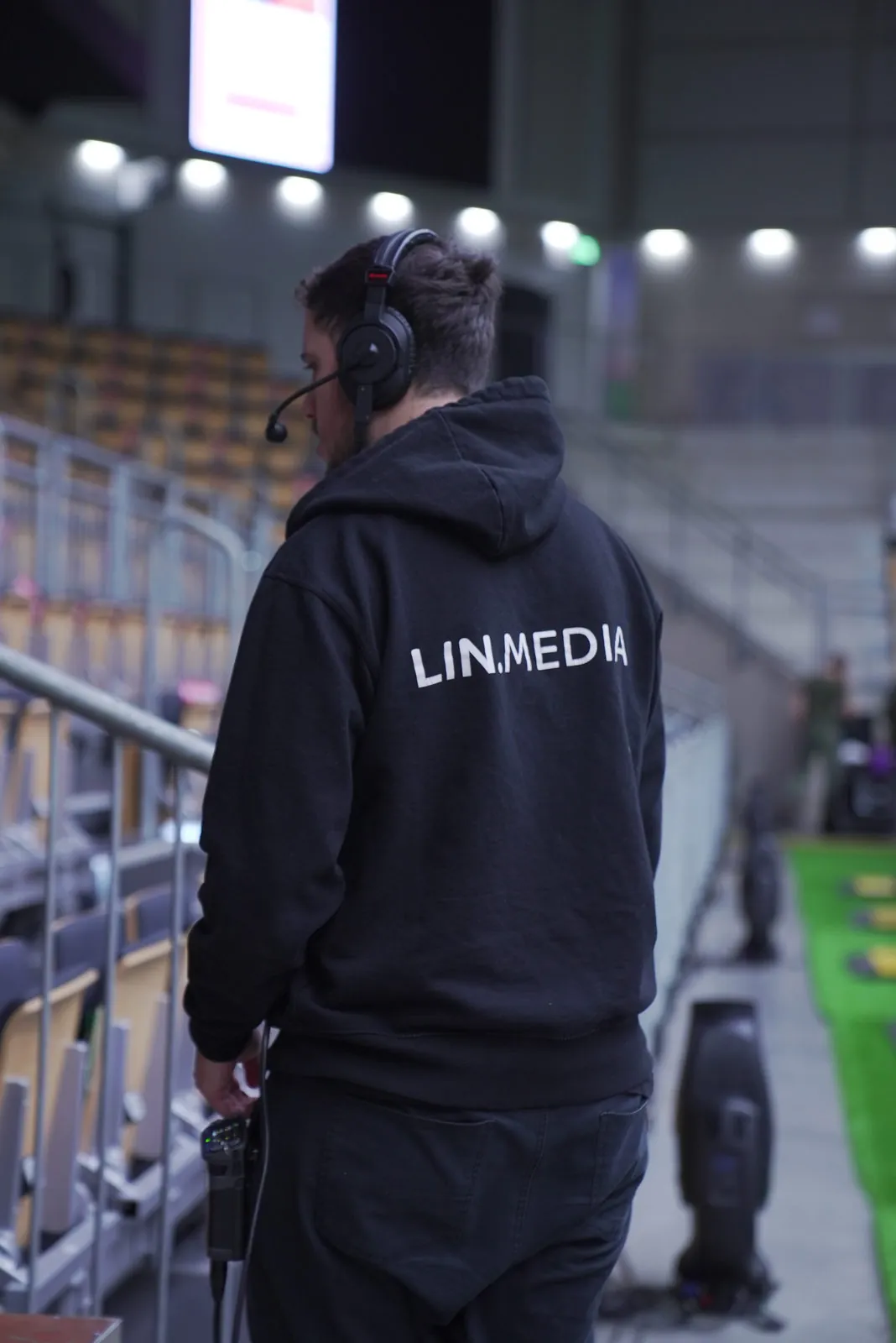 Crewmitglied im LIN.Media-Hoodie mit Headset und Funkgerät auf der Tribüne einer Halle
