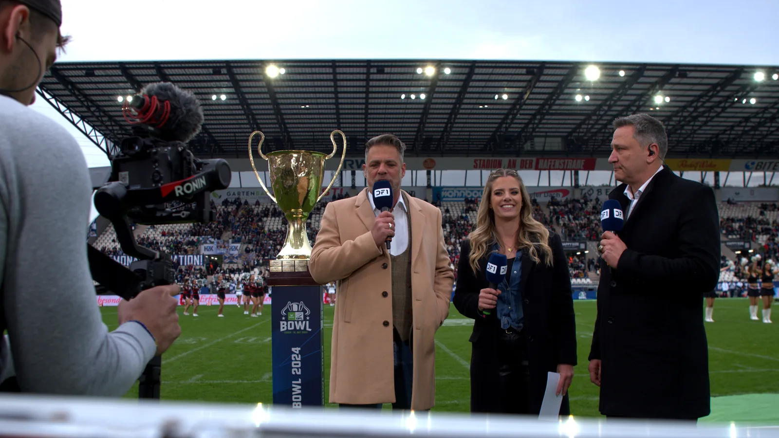Moderation am Spielfeldrand beim German Bowl: drei Moderator:innen mit Mikrofonen neben dem Pokal, links die Gimbal-Kamera von LIN.Media