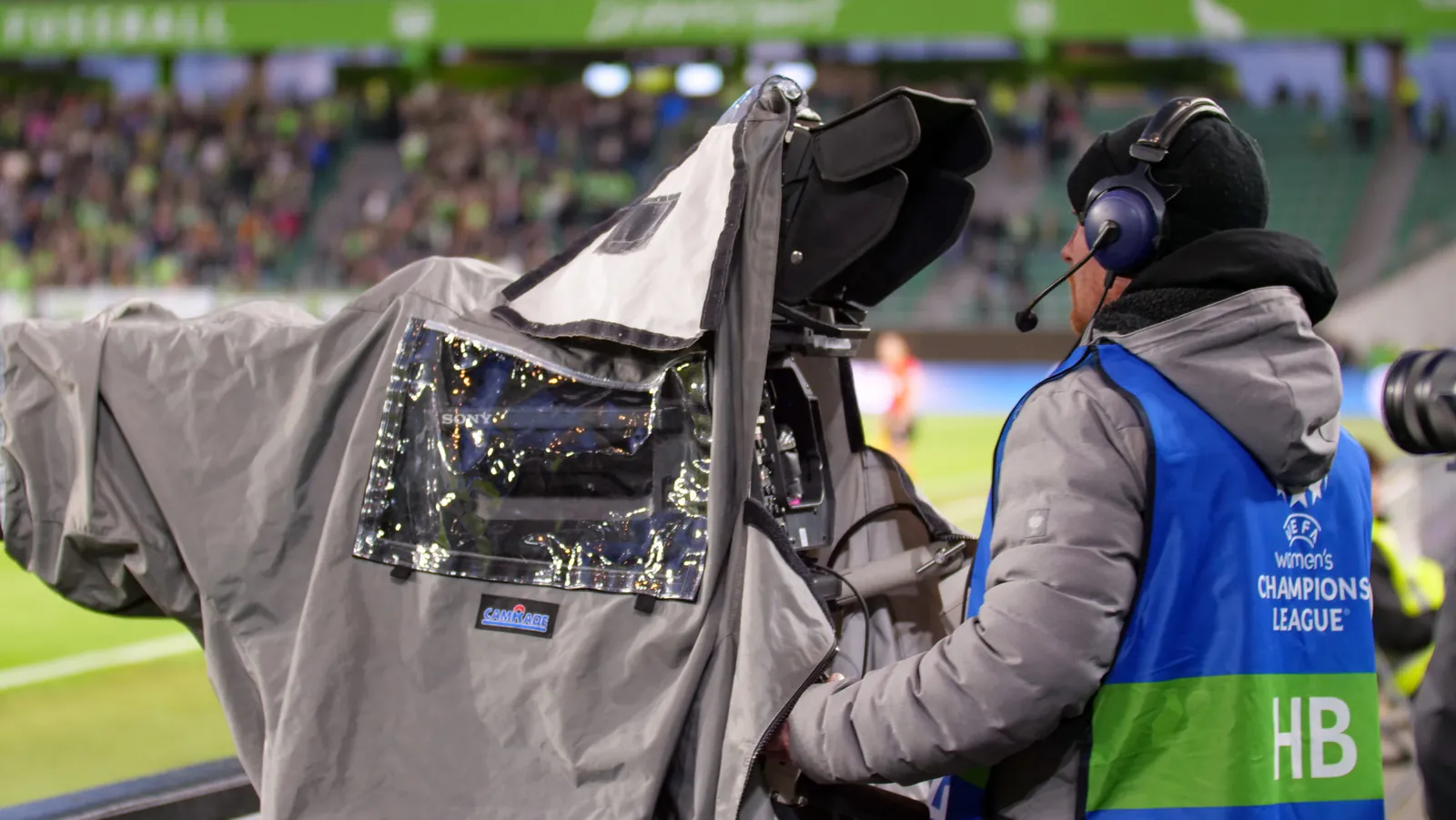 Kameramann mit Regenschutz am Spielfeldrand in Wolfsburg, Host-Broadcast-Weste